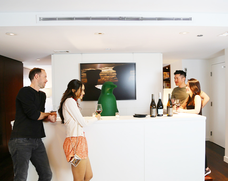 group of people surrounding bar area with wine and green penguin as bartender