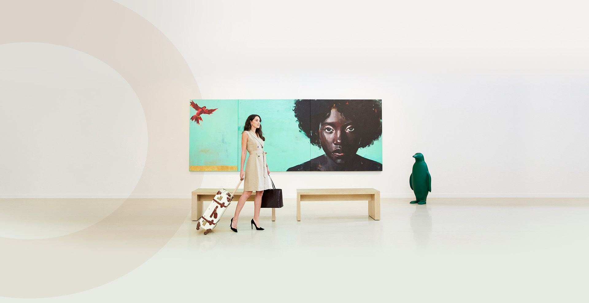 woman walking with suitcase in front of large artpiece and green penguin