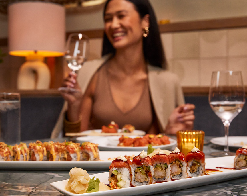 lots of sushi rolls on plates with woman laughing in the background