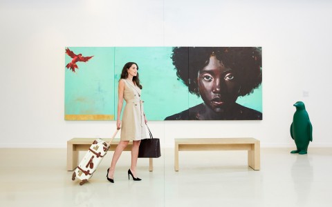 woman walking with white suitcase walking through art exhibit with green penguin