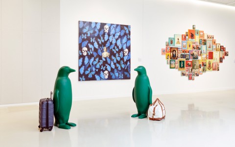 2 penguins with luggage next to them in front of butterfly mural and colorful art