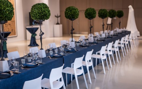 long blue meeting table with small people holding up greenery