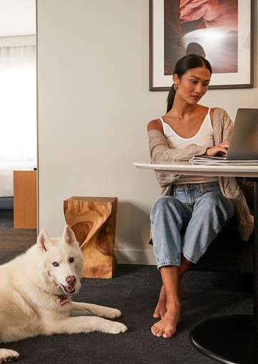 Woman typing on a computer with a white dog next to her 