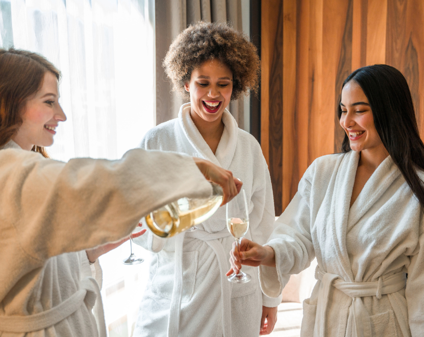 three woman wearing spa robes while drinking champagne