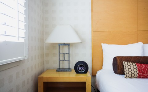 side of bed with nightstand, lamp, and alarm clock