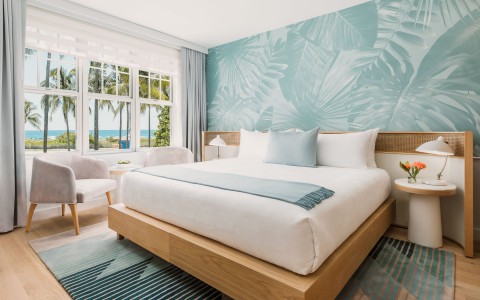 corner view of a hotel room with a queen bed and palm trees wall and white accents 