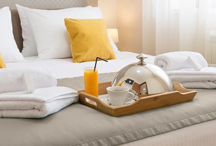 a tray with orange juice coffee and breakfast plate under a silver lid sitting on a bed