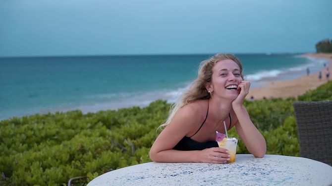 woman laughing with cocktail in her hand and ocean in the back