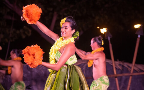 Women performing in luau with orange maracas in hand 