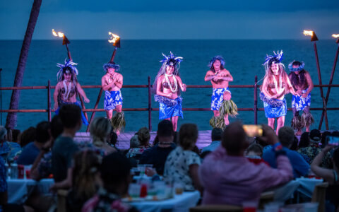 Men and Women perform in luau with oceanfront backdrop 