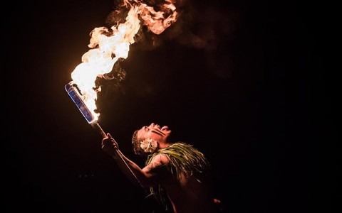 cropped shot of man in traditional luau clothing holding a fire during a dance