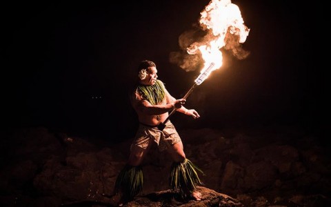 shot of man in traditional luau clothing holding a fire during a dance