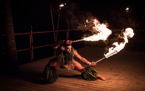 man squatting during a fire performance with two fire sticks