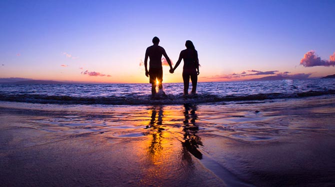 a couple holding hands while walking along the beach during sunset