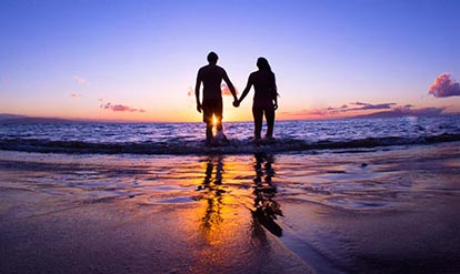 a couple holding hands while walking on a beach during the sunset