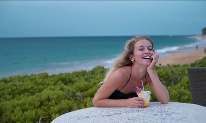 woman laughing with cocktail in her hand and ocean in the back