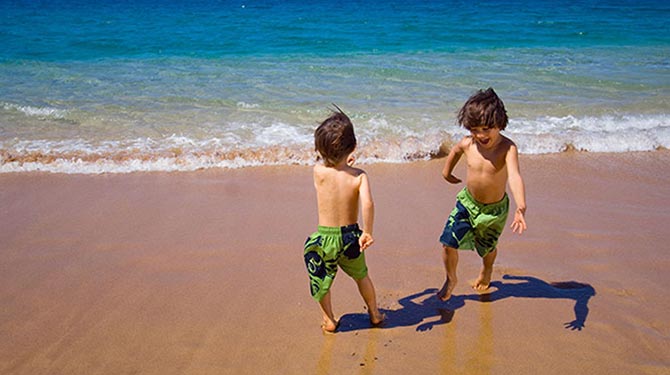 two young boys in green swim trunks playing at the shore line of a beach