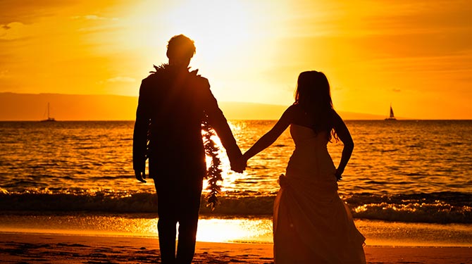 a man and a woman holding hands on the beach during sunset