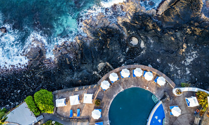 aerial view of swimming pool with umbrellas overlooking lava rock and water