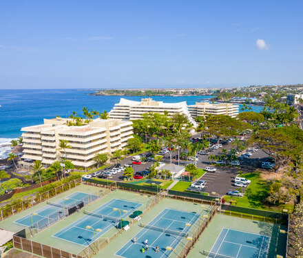 View of four tennis courts with hotel building and water in background