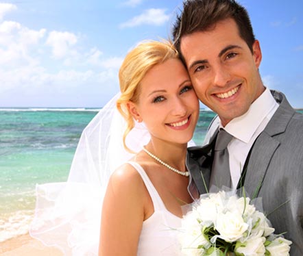 newlyweds posing in front of the beach on a sunny day