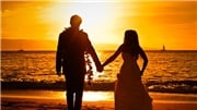 couple holding hands walking towards the ocean at sunset