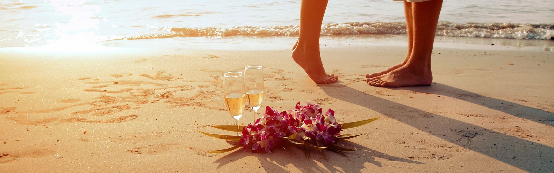 feet shot with champagne glasses on the sand next to them