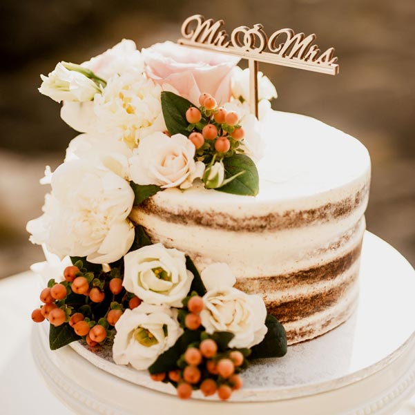 rustic wedding cake with minimal frosting and a train of flowers