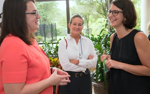 two women wearing glasses talking and a woman smiling next to them