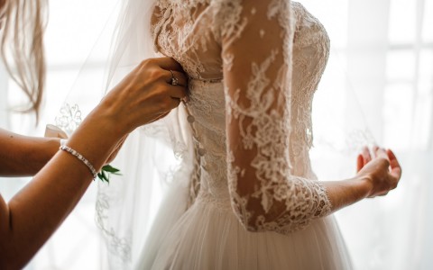 Bridesmaid buttoning brides dress
