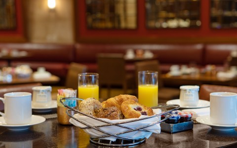basket of pastries with glasses of orange juice in the background and table setting