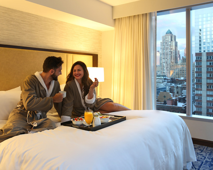 A couple eating breakfast in bed with a city view out the big window