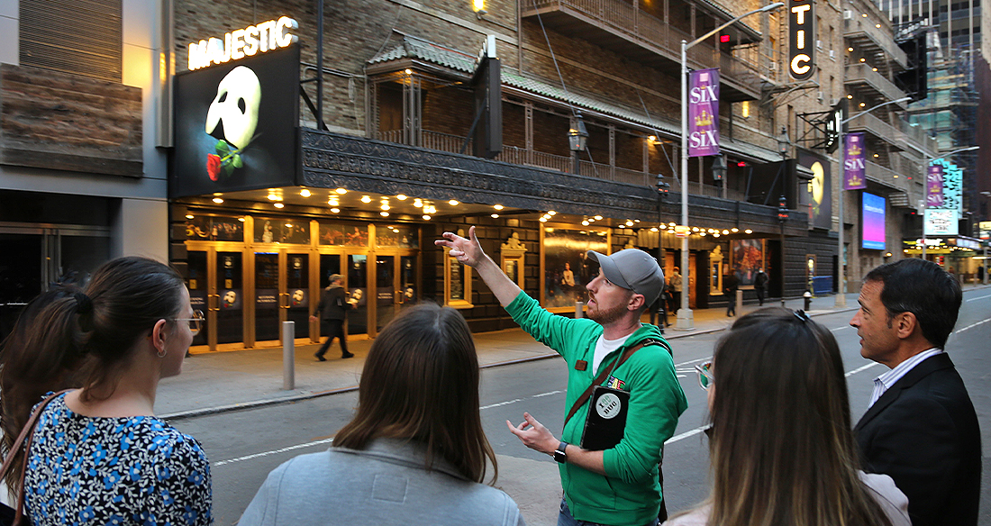 a man in a green jacket givng a broadway tour
