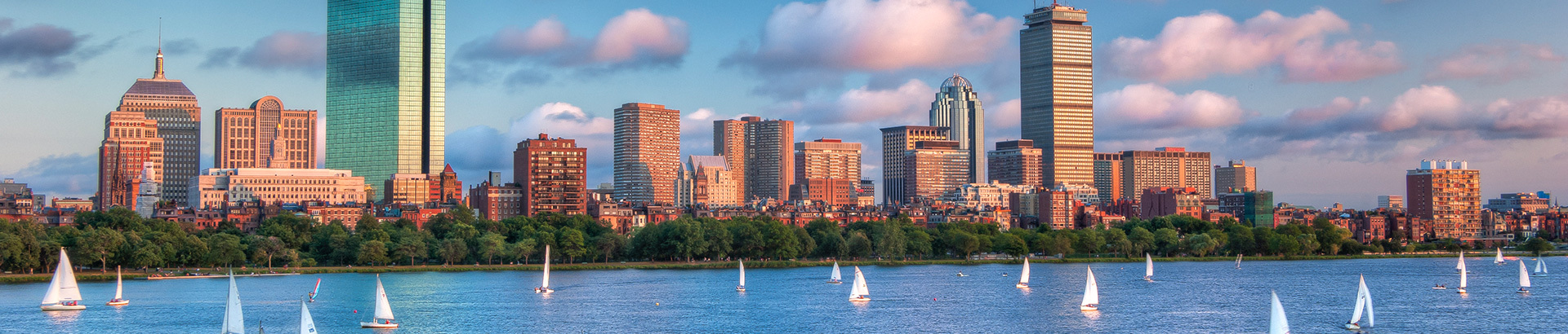 The City of Boston with the sun setting light on the buildings, and sailboats in the water