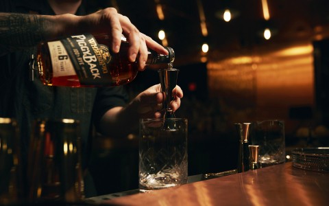 man pouring drink over the bar in glass