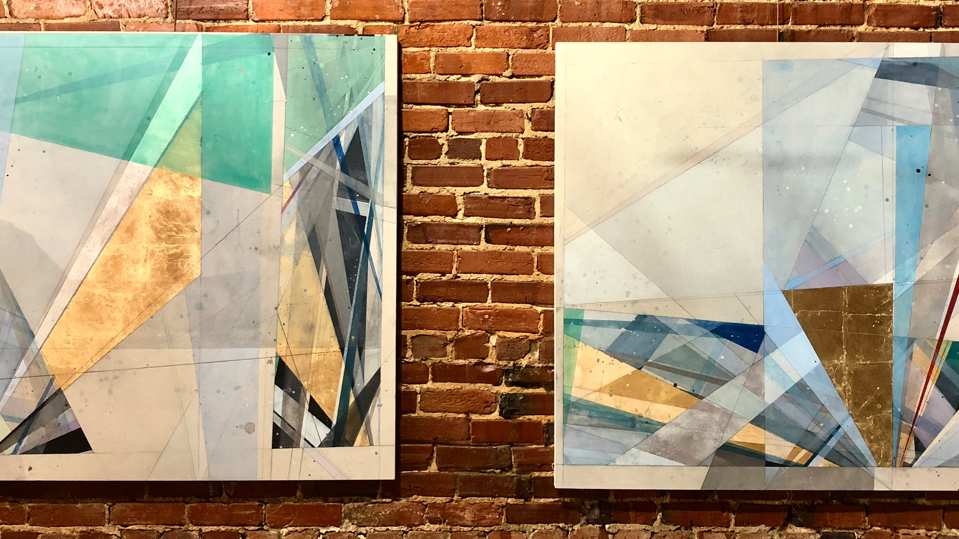 two abstract paintings hanging on a brick wall
