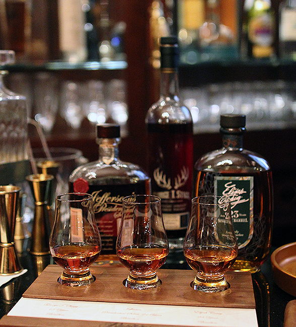 three glasses of whiskey with bottles of whiskey behind them on the bar