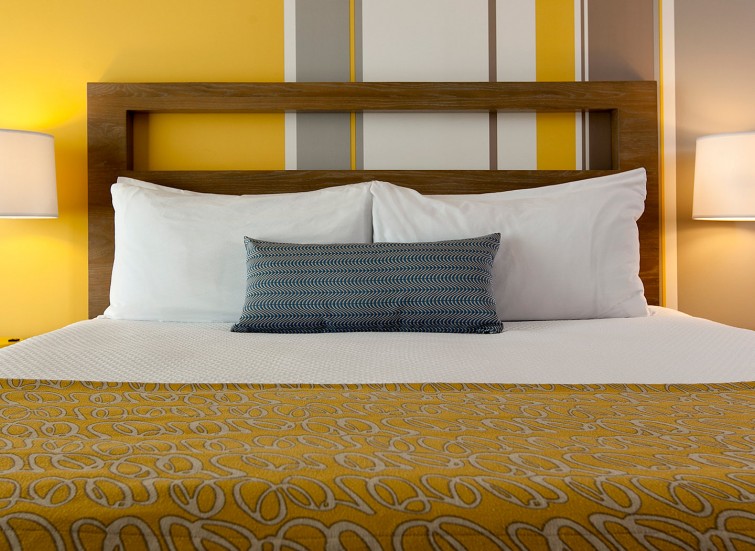 Closeup of hotel bed with striped yellow wallpaper in background