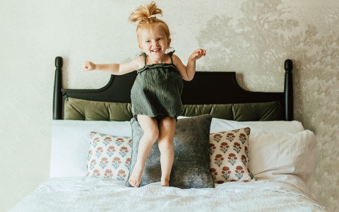 little girl in green dress jumping on bed