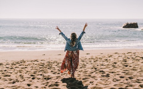 a woman with her arms up walking down the beach