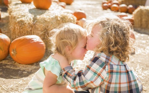 two little kids kissing on forehead in pumpkin patch