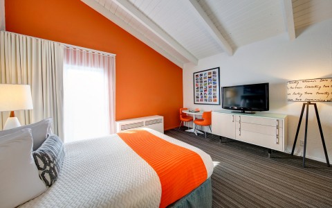 room with orange accent wall, flat screen tv, and orange throw blanket