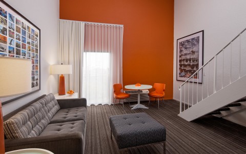 living room area with orange accent wall and dark couch and foot rest