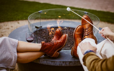 brown leather combat boots up on firepit as two people roast marshmellows