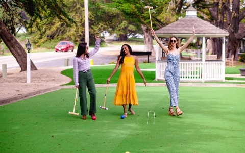 three friend playing croquet on bright green lawn