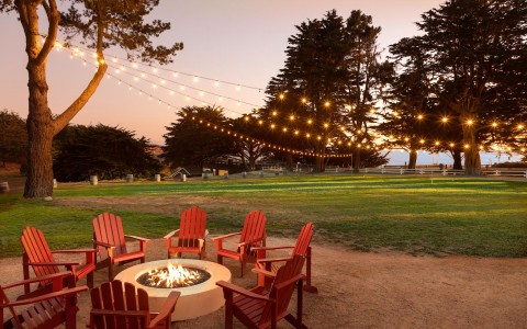 fire pit with circle of red patio chairs and twinkly lights above 