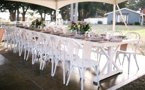 long wedding table with white chairs and pink floral arrangements