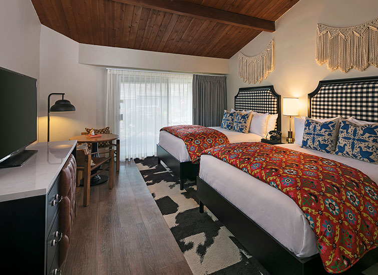 two beds with red floral throw blanket and flat screen tv