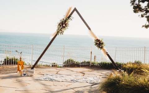 wooden triangular arch with flower bouquets for wedding with an ocean view 