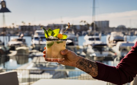 person in red long sleeve holding cocktail drink with marina backdrop